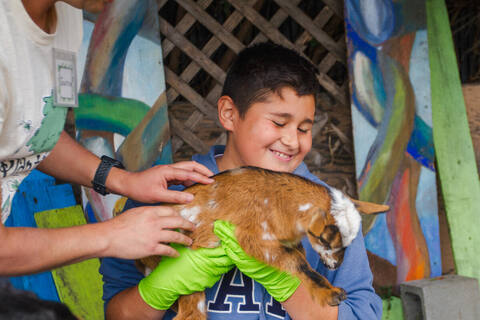 Boy in green gloves holding a baby goat
